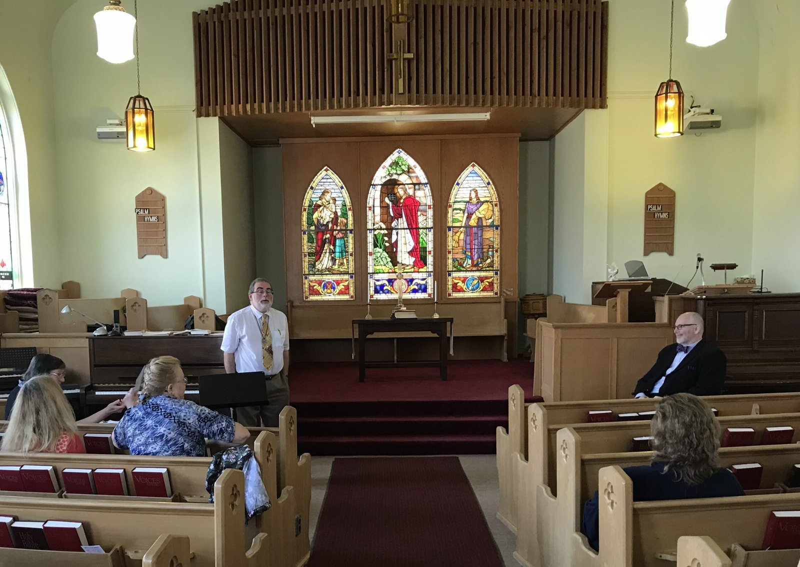 A Sunday church service in progress inside the sanctuary at Wesley United Church in Stoney Creek, featuring beautiful stained glass windows behind the altar.